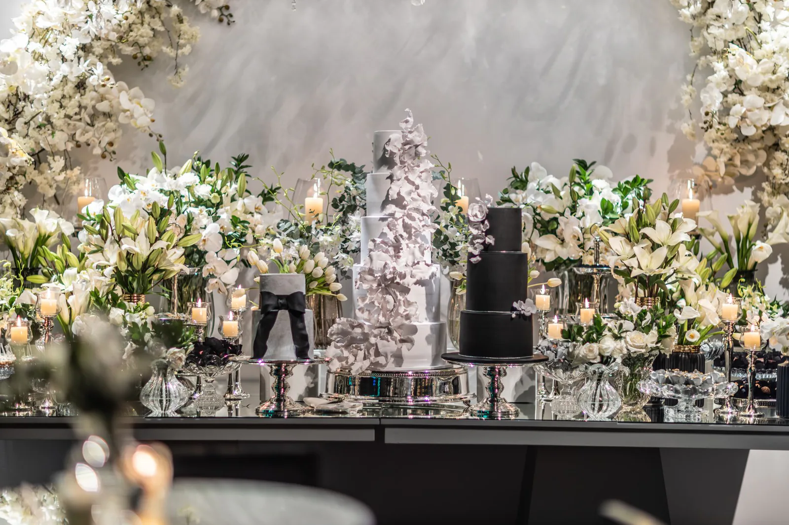 Tiered wedding cake surrounded by lush floral arrangements